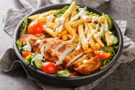 Photo for Pittsburgh steak salad consists of a bed of lettuce that's topped with tomatoes, cucumbers, a piece of grilled chicken, and crispy french fries closeup on the bowl on the table. Horizonta - Royalty Free Image