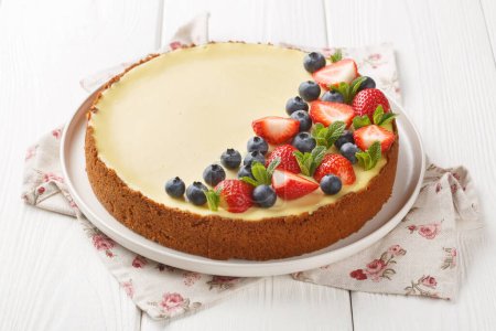 Téléchargez les photos : New York cheesecake est un dessert qui est une tarte ouverte ou même un gâteau décoré avec des baies fraîches gros plan sur l'assiette sur la table en bois. Horizonta - en image libre de droit