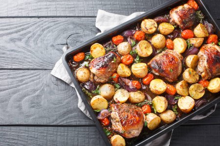 Téléchargez les photos : Poulet balsamique barbecue italien avec pommes de terre, oignon rouge et tomates en gros plan sur une plaque à pâtisserie sur une table en bois. Vue de dessus horizontale d'en haut - en image libre de droit