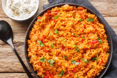 Traditional turkish meyhane pilavi bulgur pilaf with tomato sause close-up on a plate on a wooden table. Horizontal top view from abov