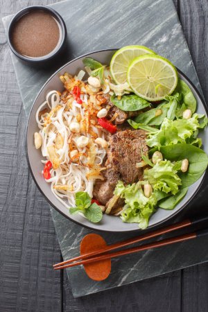 Photo for Vietnamese Beef Noodle Salad Pho Tron closeup on the plate on the wooden table. Vertical top view from abov - Royalty Free Image