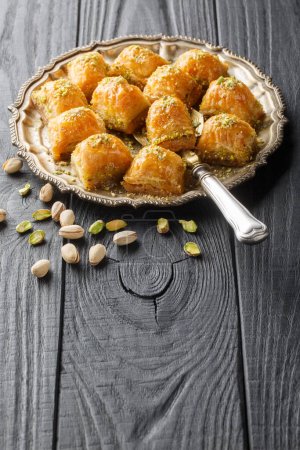 Foto de Baklava turca con mantequilla, hojaldre escamoso empapado en miel y azúcar con pistachos tiernos rellenos entre capas de masa de primer plano en el plato de la mesa de madera. Vertica - Imagen libre de derechos