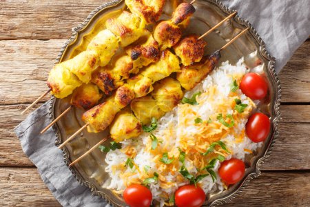 Der persische Jujeh Kabab ist ein iranisches Gericht, das aus gegrillten Hühnerstücken besteht, die in Safran mariniert sind, und Joghurt, der mit Reis in Großaufnahme auf dem Teller auf dem Tisch serviert wird. Horizontale Ansicht von oben