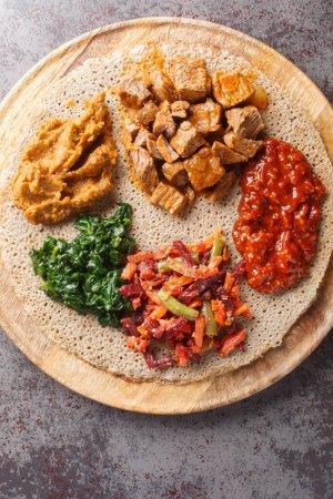 Photo for Mix of vegetables and stews on injera flatbread close up on the wooden board on the table. Vertical top view from abov - Royalty Free Image