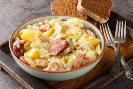 Téléchargez les photos : Dans un bol sur la table, le chou de Hunter mijoté avec des saucisses, des pommes de terre, du bacon et des oignons. Horizonta - en image libre de droit