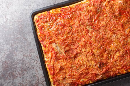 Photo for Sfincione Palermitano is a thick pizza topped with strong flavors like anchovies, caciocavallo cheese, onions and tomato sauce closeup on the baking sheet on the table. Horizontal top view from abov - Royalty Free Image