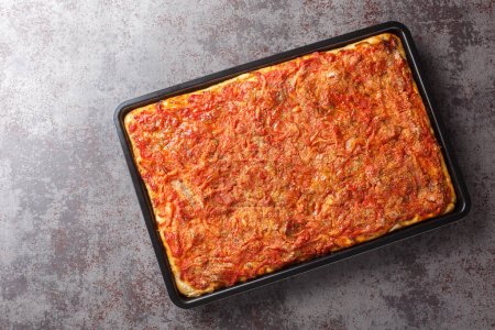 Foto de Pizza rectangular Sfincione con cebolla, tomate, queso, anchoas y pan rallado de cerca en una bandeja para hornear sobre la mesa. Vista superior horizontal desde arriba - Imagen libre de derechos