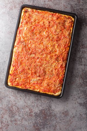 Photo for Delicious Italian Sfincione focacia with onions, tomatoes, cheese, anchovies and breadcrumbs closeup on a baking sheet on the table. Vertical top view from abov - Royalty Free Image