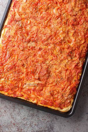 Photo for Sicilian Pizza made with a thick soft rectangular pizza crust, a tomato sauce, onions, anchovies and topped with breadcrumbs closeup on the baking sheet on the table. Vertical top view from abov - Royalty Free Image