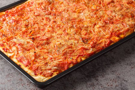 Photo for Rectangular Sfincione pizza with onions, tomatoes, cheese, anchovies and breadcrumbs closeup on a baking sheet on the table. Horizonta - Royalty Free Image