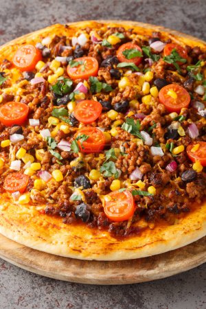 Tex Mex Taco-Pizza mit Hackfleisch, Tomaten, Mais, schwarzen Bohnen, Cheddar-Käse, roten Zwiebeln und mexikanischen Gewürzen in Großaufnahme auf einem Holzbrett auf dem Tisch. Vertica