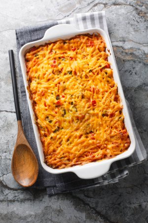 King Ranch Chicken Casserole with pulled chicken, corn tortillas, shredded cheese, peppers, and spicy green chiles close-up in a baking dish on a marble table. Vertical top view from abov