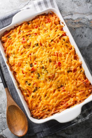 King Ranch Chicken Casserole combines juicy chicken, colorful peppers, tortillas in a bubbly creamy cheesy sauce close-up in a baking dish on a marble table. Vertical top view from abov