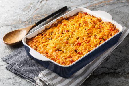 King Ranch Casserole layers of juicy chicken, corn tortillas and cheese enveloped in a cream sauce with tomatoes, bell peppers and green chiles close-up in a baking dish on a marble table. Horizonta