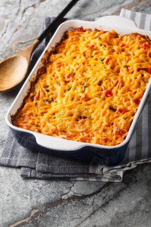 King Ranch Chicken Casserole with pulled chicken, corn tortillas, shredded cheese, peppers, and spicy green chiles close-up in a baking dish on a marble table. Vertica