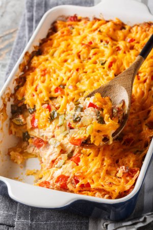 Classic King Ranch chicken casserole is bursting with chicken, corn tortillas, tomatoes, peppers, and cheesy goodness close-up in a baking dish on a marble table. Vertica