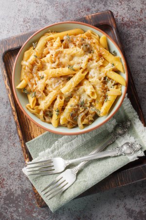 One Pot French Onion Pasta is rich and creamy, with sweet caramelized onions and penne closeup on the bowl on the wooden board. Vertical top view from abov