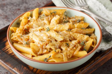 Delicious French onion pasta penne with caramelized onions, fragrant thyme, garlic and gruyere cheese close-up on a bowl on a wooden board. Horizonta
