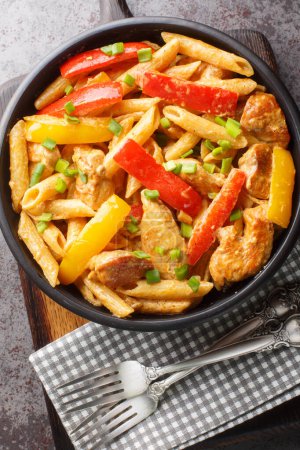 Rasta pasta is a very colorful dish consisting of grilled chicken, a combination of different bell peppers, a thick coconut sauce and Caribbean spices close-up. Vertical top view from abov