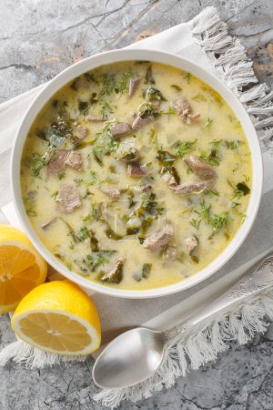 Tasty Greek Easter soup with lamb offal, herbs, seasoned with egg and lemon sauce close-up in a bowl on a marble table. Vertical top view from abov