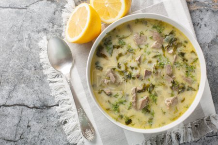 Magiritsa Greek Easter soup with lamb intestines and liver, herbs, seasoned with egg and lemon sauce close-up in a bowl on a marble table. Horizontal top view from abov