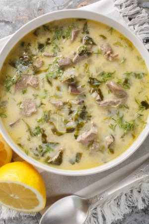 Greek Easter soup Magiritsa with lamb offal, herbs, seasoned with egg and lemon sauce close-up in a bowl on a marble table. Vertical top view from abov