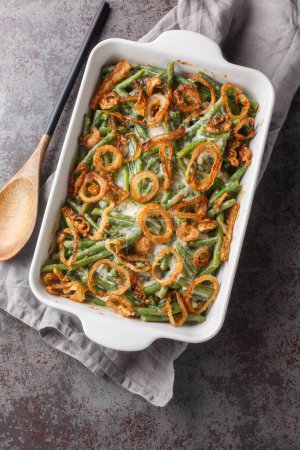 Close-up of Green Bean Casserole topped with crispy fried onions on the baking dish on the table. Vertical top view from abov