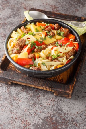 Lagman-Suppe mit Rindfleisch, Nudeln, Paprika, Kartoffeln, Karotten, Zwiebeln und Kräutern in Großaufnahme auf dem Teller auf dem Holzbrett. Vertica