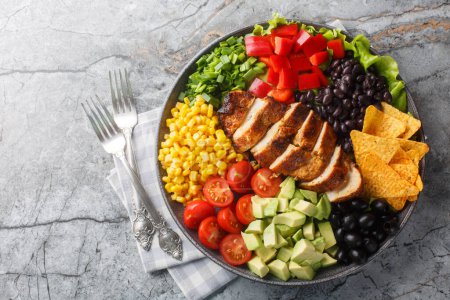 Photo for Southwest salad of chicken, corn, peppers, olives, avocado, tomatoes and onions close-up on a board on the table. Horizontal top view from abov - Royalty Free Image