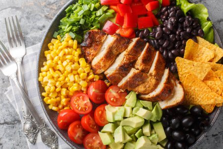 Photo for Southwest salad of chicken, corn, peppers, olives, avocado, tomatoes and onions close-up on the plate on the table. Horizontal top view from abov - Royalty Free Image