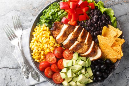Photo for Tex-Mex Santa Fe chicken salad with lettuce, tomatoes, corn, black beans, pepper, avocado, olive closeup on the plate on the table. Horizontal top view from abov - Royalty Free Image