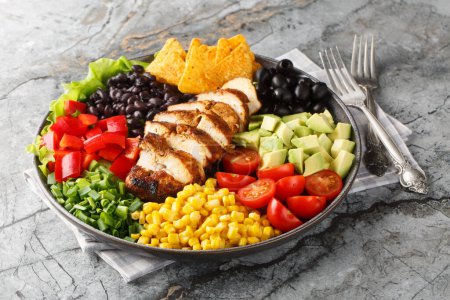Foto de La ensalada del suroeste del pollo, el maíz, los pimientos, las aceitunas, el aguacate, los tomates y la cebolla se acercan a la tabla sobre la mesa. Horizonta - Imagen libre de derechos