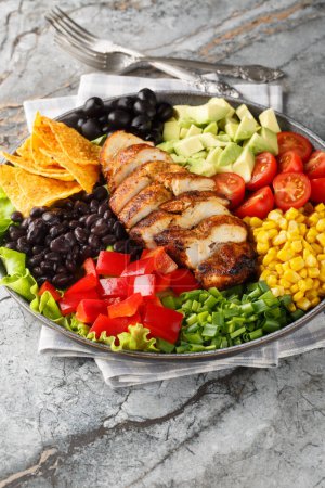 Photo for Santa Fe salad combines lettuce, tomatoes, corn, black beans, pepper, avocado, olive and chicken closeup on the plate on the table. Vertica - Royalty Free Image