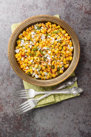 Homemade Mexican Street Corn Esquites Salad with jalapeno, cilantro, Cotija cheese, onion and spices seasoned with sour cream close-up on the plate on the table. Vertical top view from abov