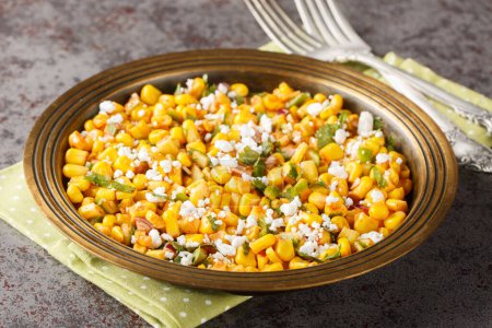 Esquites salad is a grilled Mexican corn that is slathered with a creamy sauce, seasoned with chile powder and lime juice and topped with Cotija cheese close-up on the plate on the table. Horizonta
