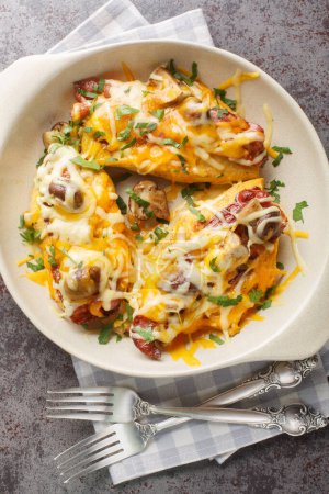 Tasty baked chicken breast in honey mustard sauce, topped with mushrooms, bacon, and a pile of cheese closeup in the baking dish on the table. Vertical top view from abov