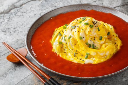 Leckeres asiatisches Tornado-Omelette mit Sesam, grünen Zwiebeln und scharfer Paprika-Sauce in Großaufnahme in einem Teller auf dem Tisch. Horizonta
