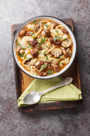 Creamy Beef Stroganoff Soup is made with tender chunks of beef, mushrooms and noodles in an extra-delicious broth in a bowl on the table. Vertical top view from abov