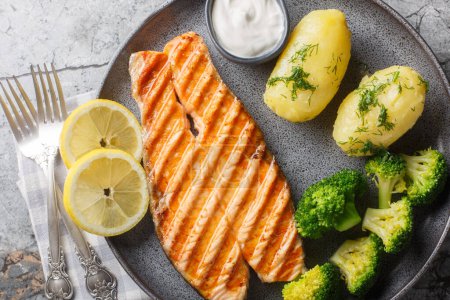 Grilled salmon, boiled potatoes, broccoli and cream sauce in a plate on the table. Horizontal top view from abov