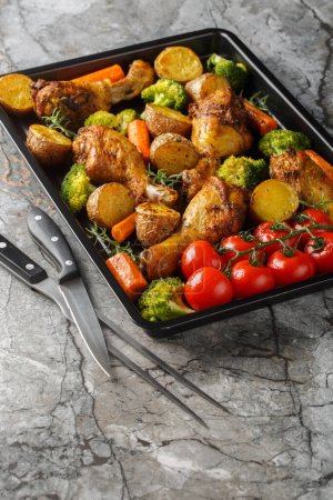Homemade baked chicken drumsticks with vegetables and rosemary close-up on a baking sheet on the table. Vertica
