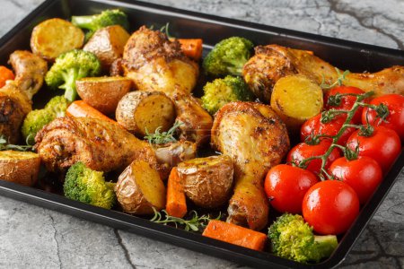 BBQ baked chicken drumsticks with seasonal vegetables and rosemary close-up on a baking sheet on the table. Horizonta