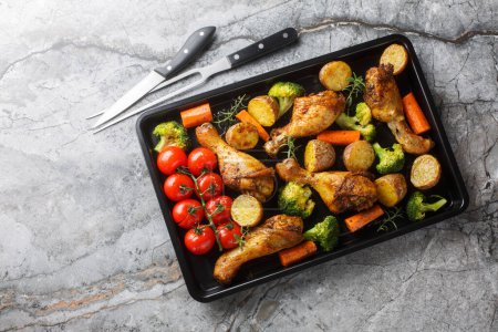 BBQ baked chicken drumsticks with seasonal vegetables and rosemary close-up on a baking sheet on the table. Horizontal top view from abov