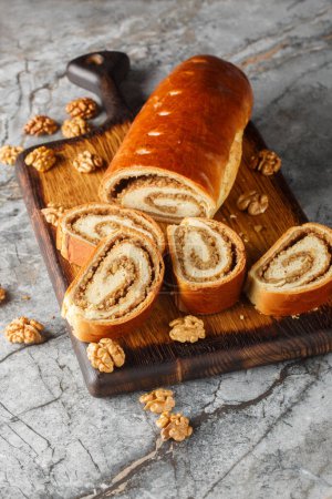 Nut roll is a pastry consisting of a sweet yeast dough with a nut paste made from ground nuts and honey closeup on the wooden board on the table. Vertica