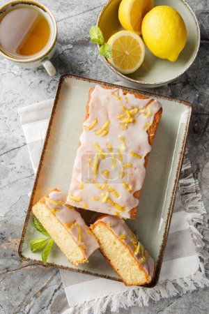 Lemon loaf cake, classic recipe, decorated with sugar icing closeup on the plate on the table. Vertical top view from abov