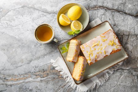 Lemon drizzle cake with lemon zest and icing is a classic British tea-time treat closeup on the plate on the table. Horizontal top view from abov