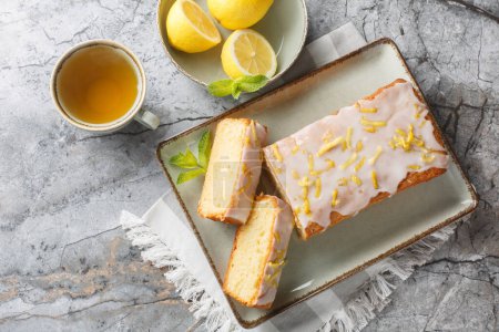 Homemade glazed lemon pound cake closeup on the plate served with tea on the table. Horizontal top view from abov