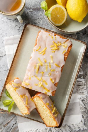 Lemon Drizzle Cake is a classic British cake known for its moist texture and vibrant lemon flavour closeup on the plate on the table. Vertical top view from abov