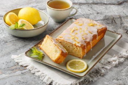 Homemade glazed lemon pound cake closeup on the plate served with tea on the table. Horizonta