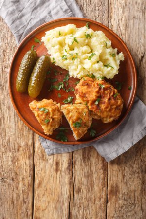 Dutch Schnitzel or Holandsky rizek in Czech, is a combination of delicious pork meat with shredded cheese, herbs served with mashed potatoes closeup on the plate on the table. Vertical top vie