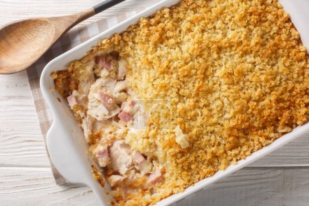 Chicken Cordon Bleu casserole layered together, it's a warm and comforting weeknight meal close up in the baking dish on the white wooden table. Horizontal top view from abov